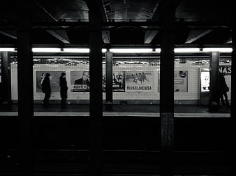Black and white subway platform with commuters and advertisements
