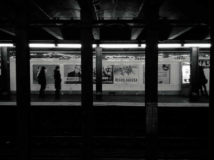 Black and white subway platform with commuters and advertisements
