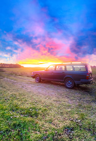 Vintage station wagon parked in field at sunset