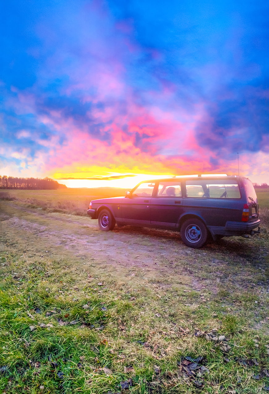 Vintage station wagon parked in field at sunset