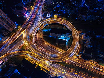 Aerial night view of circular highway interchange with light trails