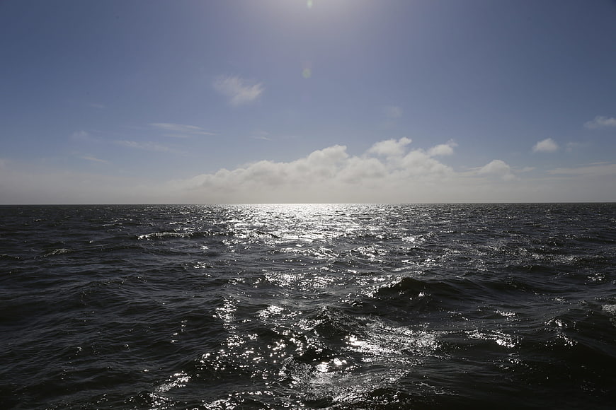 Sunlight Sparkling on Dark Ocean Waves Under Blue Sky