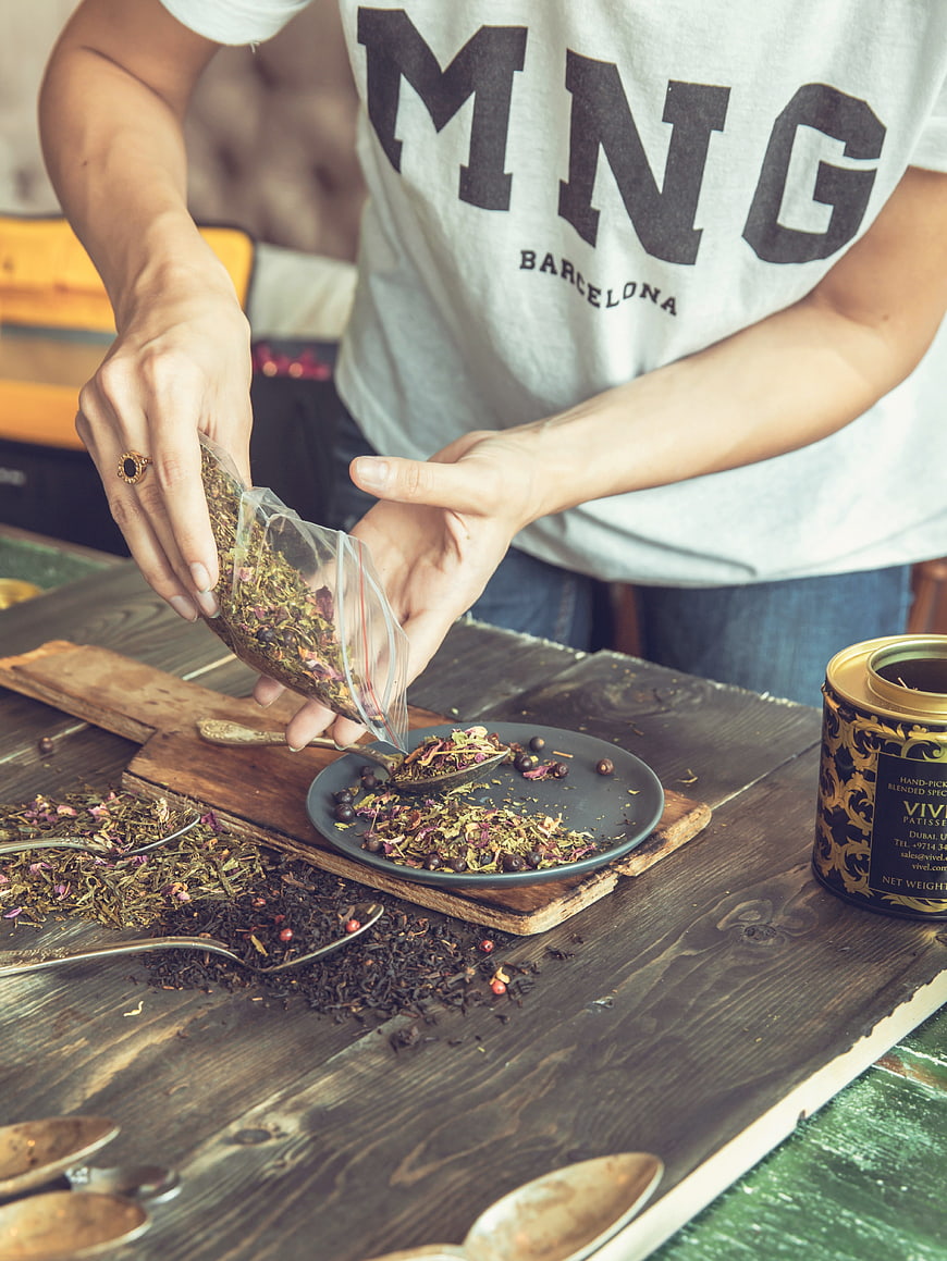 Woman pouring herbal tea blend onto wooden table