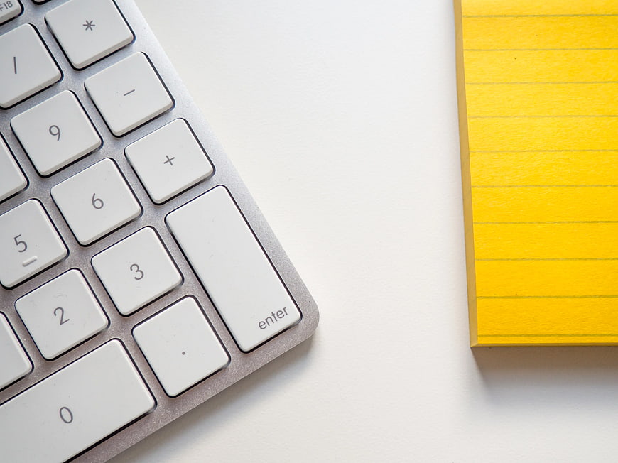 White Keyboard and Yellow Notepad on Desk
