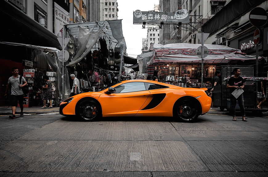 Orange McLaren sports car parked on busy Hong Kong street
