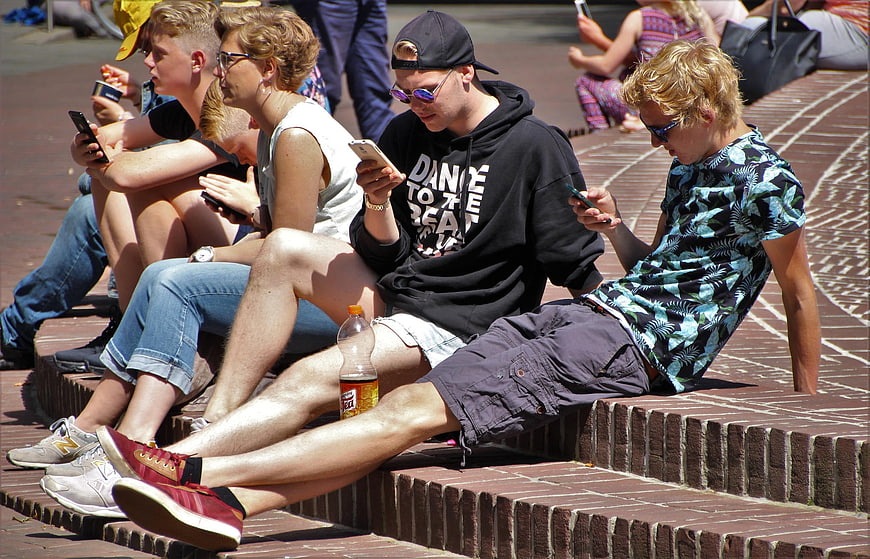 Teenagers sitting on brick steps playing mobile games
