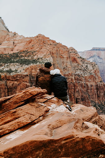 Couple sitting on red rock cliff overlooking canyon