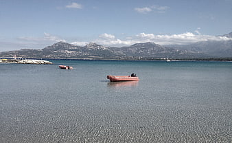 Red inflatable boat floating in calm sea with mountains