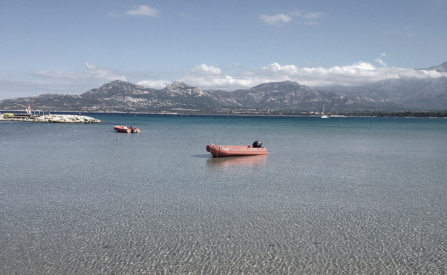 Red inflatable boat floating in calm sea with mountains