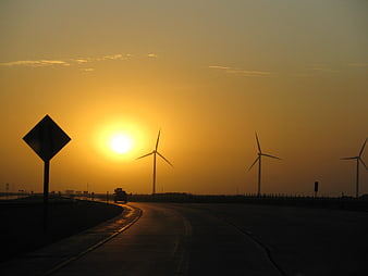 Silhouette of wind turbines on highway at golden sunset
