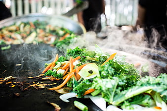 Steaming kale and carrots grilling on a large flat top