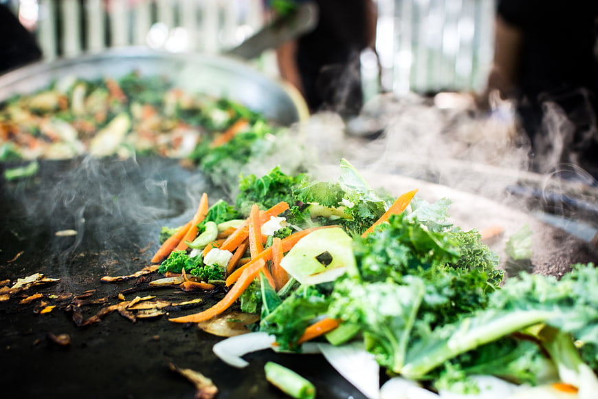 Steaming kale and carrots grilling on a large flat top