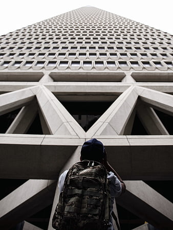 Low angle view of man with backpack looking up at skyscraper