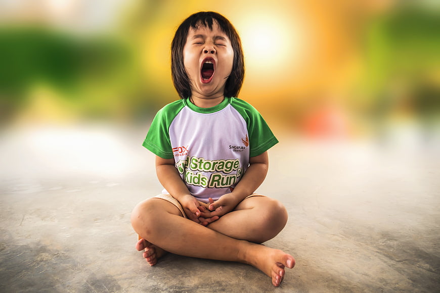 Cute little girl yawning while sitting cross-legged outdoors