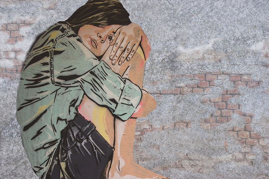 Street Art Mural of Woman Hugging Her Knees on Weathered Brick Wall