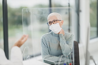 Senior woman wearing face mask behind plexiglass barrier