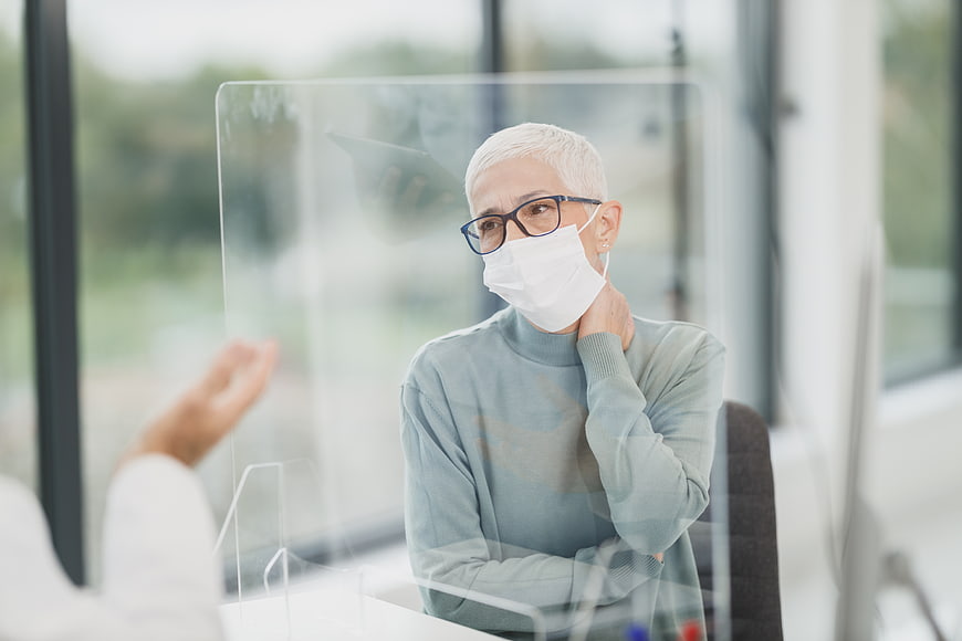 Senior woman wearing face mask behind plexiglass barrier