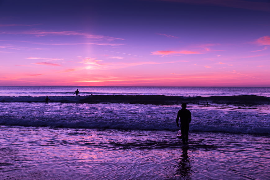 Surfer Silhouette Walking into Ocean at Vibrant Purple Sunset