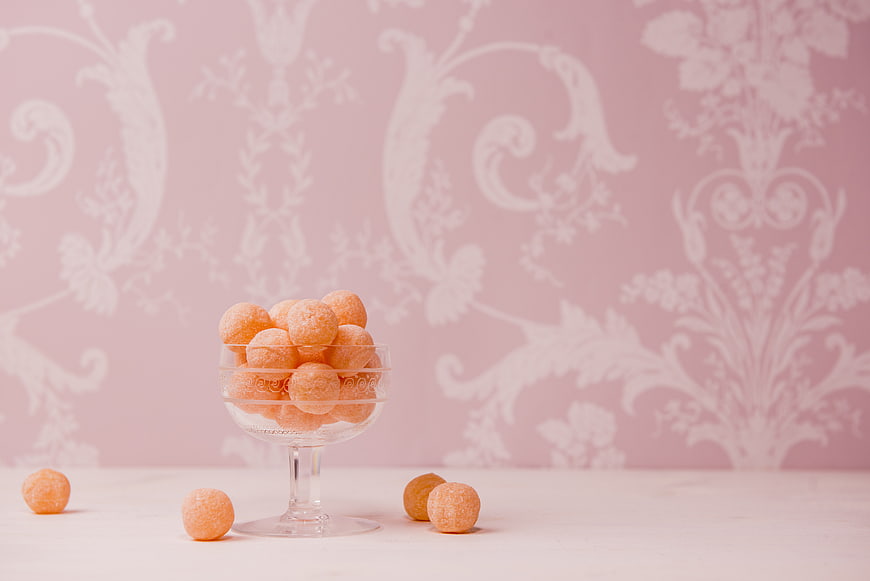 Orange sugar-coated candies in glass bowl on pink background