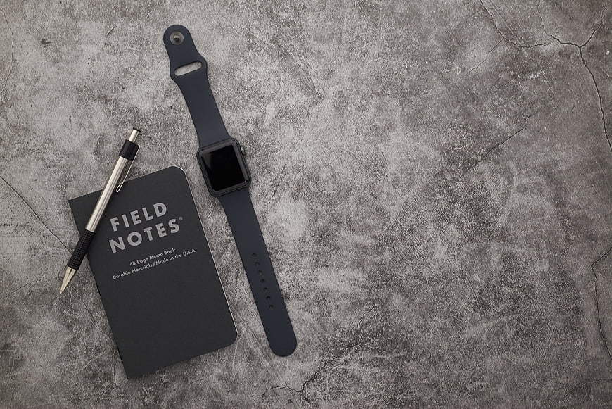 Minimalist flat lay of smartwatch, notebook, and pen on concrete