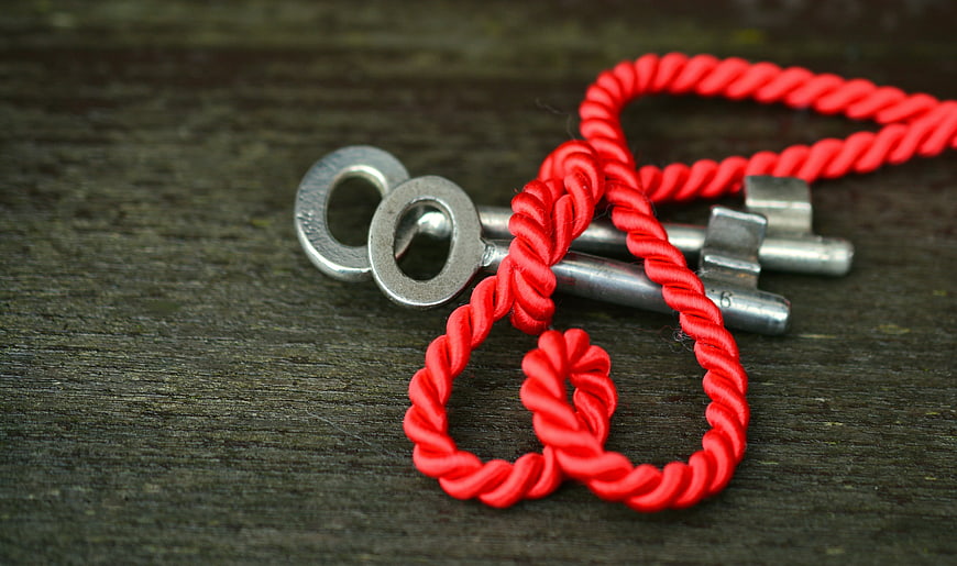 Silver Keys Tied With Red Cord On Dark Wood