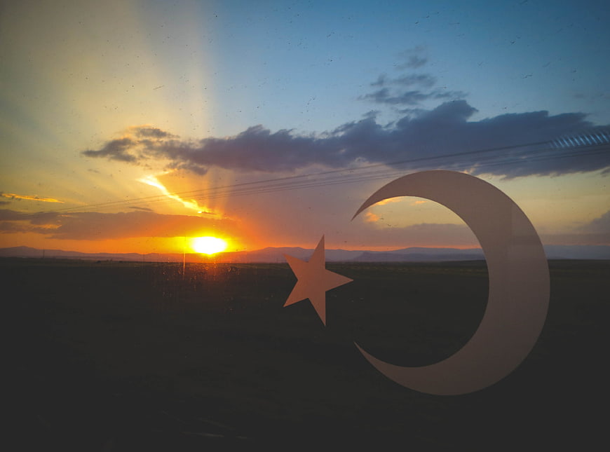 Crescent moon and star silhouette against sunset landscape