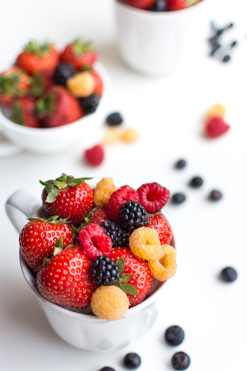 Fresh mixed berries in white teacup on white background