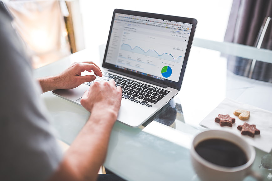 Man typing on laptop with analytics charts and coffee