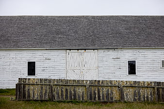 Weathered white wooden barn with rustic fence and gray roof