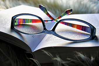 Black eyeglasses with rainbow reflections resting on an open book