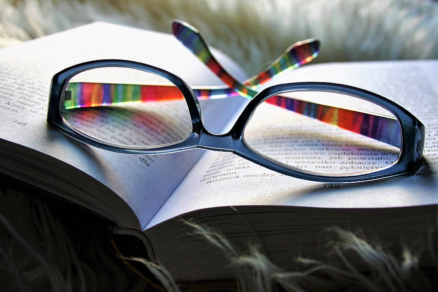 Black eyeglasses with rainbow reflections resting on an open book
