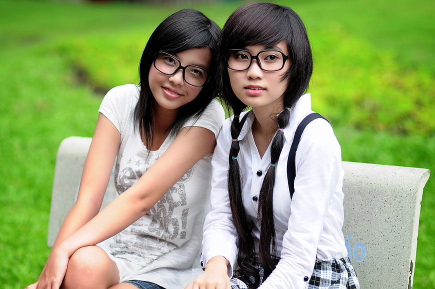 Two Young Women with Glasses Sitting on Park Bench