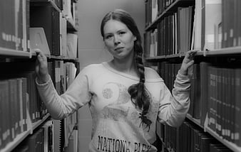 Young woman with braid browsing books in library aisle