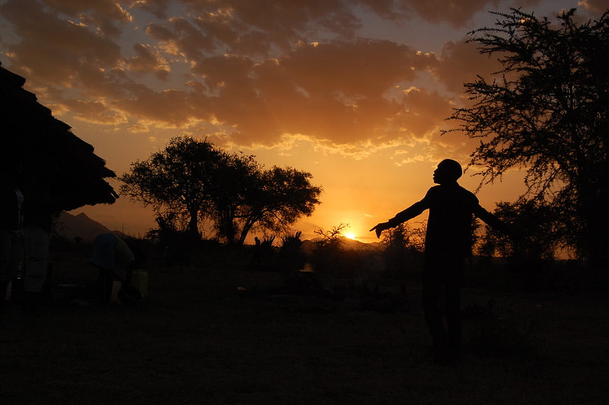 Silhouette of man with arms outstretched at sunset in rural village