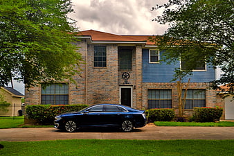 Blue Lincoln MKZ sedan parked in front of a two-story brick and blue siding suburban house