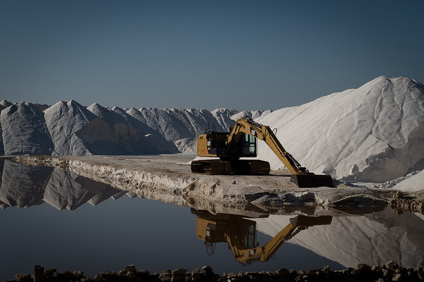 Yellow Excavator Mining Salt Ponds with Reflection