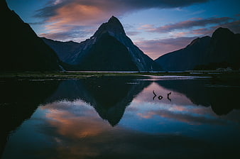 Misty mountain peak reflection in calm lake at twilight