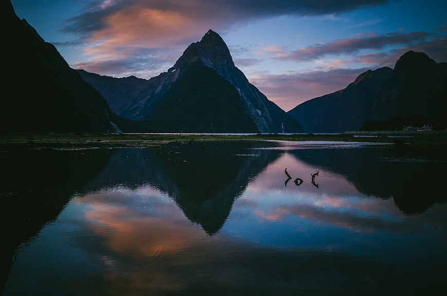 Misty mountain peak reflection in calm lake at twilight