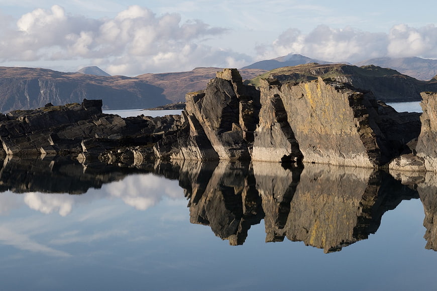 Dramatic rocky outcrop reflected in calm Scottish loch water