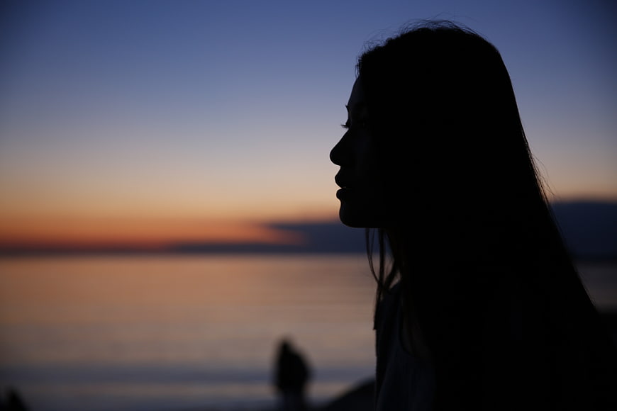 Silhouette of a woman in profile against a sunset ocean horizon