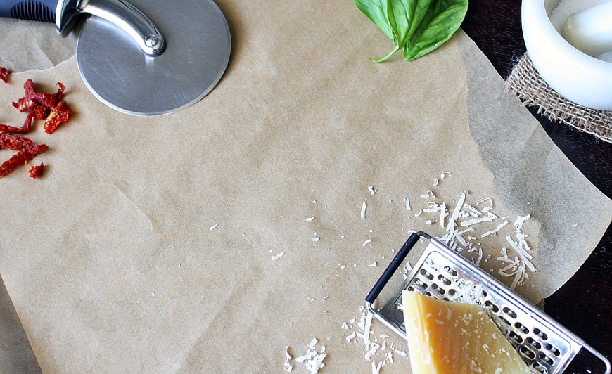 Pizza ingredients on parchment paper with grater and cutter