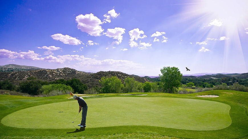 Golfer Putting on Green Course with Hills and Blue Sky