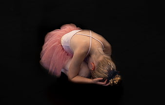 Young ballerina in pink tutu performing a deep floor bend on black background