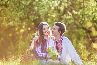 Young couple in traditional embroidered shirts sitting in a sunny meadow