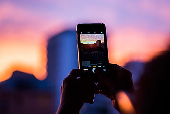 Hands holding smartphone capturing city sunset