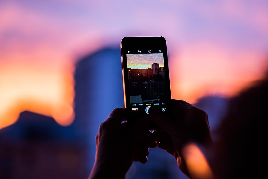 Hands holding smartphone capturing city sunset