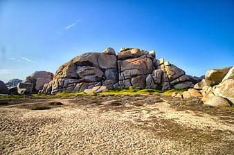 Granite boulders on sandy terrain under blue sky