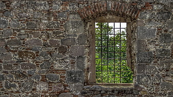 Ancient stone wall with arched window and metal bars