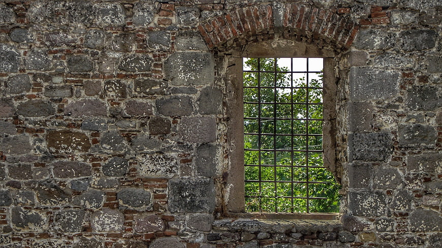 Ancient stone wall with arched window and metal bars