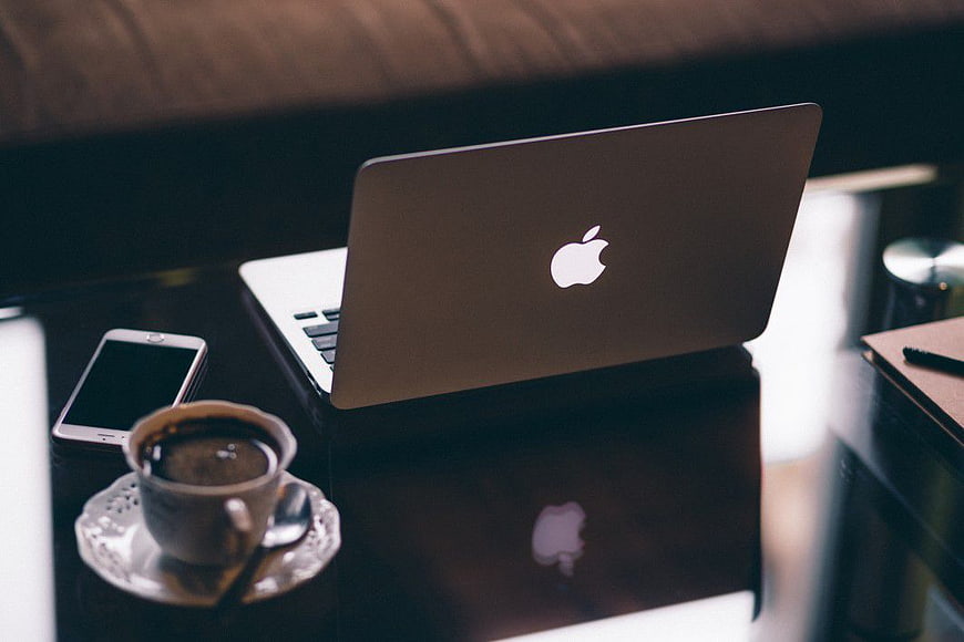 MacBook laptop, smartphone, and coffee on dark desk